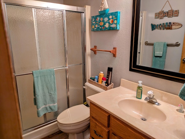 bathroom featuring toilet, a stall shower, vanity, and a textured wall