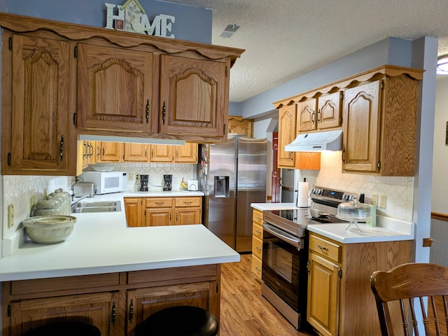 kitchen featuring a peninsula, light wood-style flooring, stainless steel appliances, light countertops, and under cabinet range hood