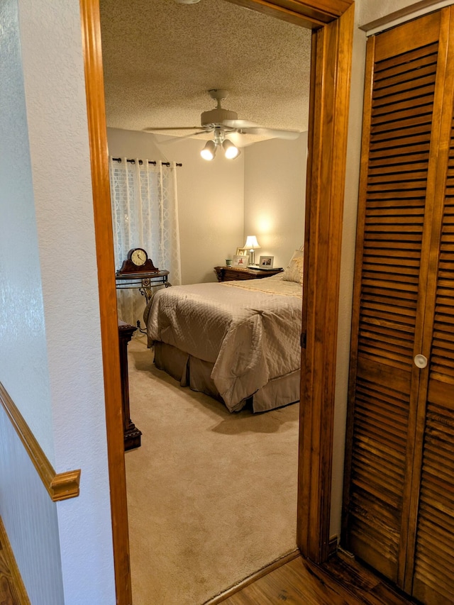 carpeted bedroom featuring wood finished floors, a textured wall, a closet, a textured ceiling, and a ceiling fan