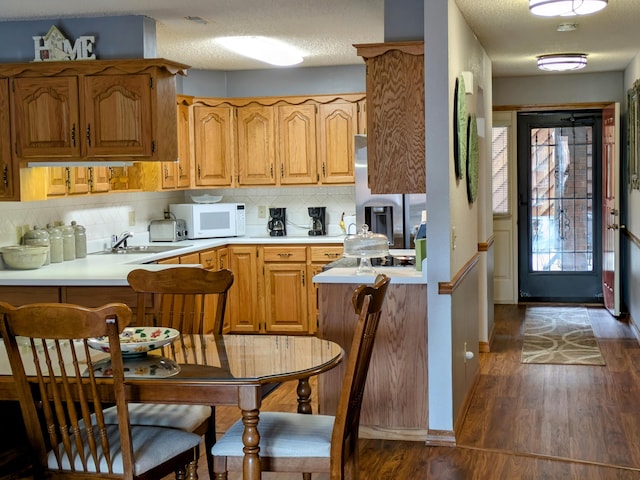 kitchen featuring dark wood-type flooring, white microwave, stainless steel fridge, and a peninsula