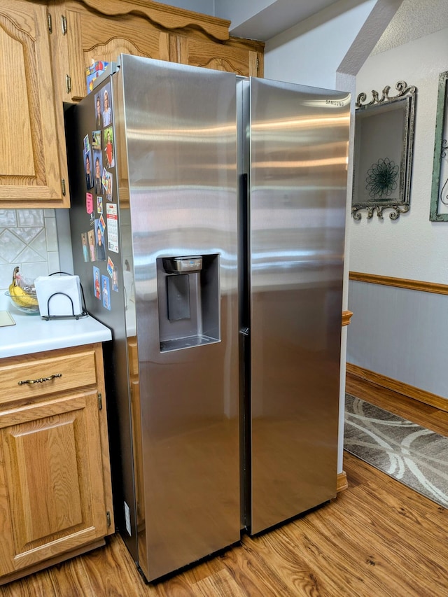 kitchen with light wood finished floors, decorative backsplash, light countertops, and stainless steel refrigerator with ice dispenser