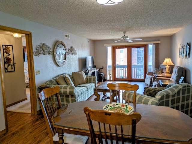 living area featuring visible vents, a textured ceiling, wood finished floors, ceiling fan, and a textured wall