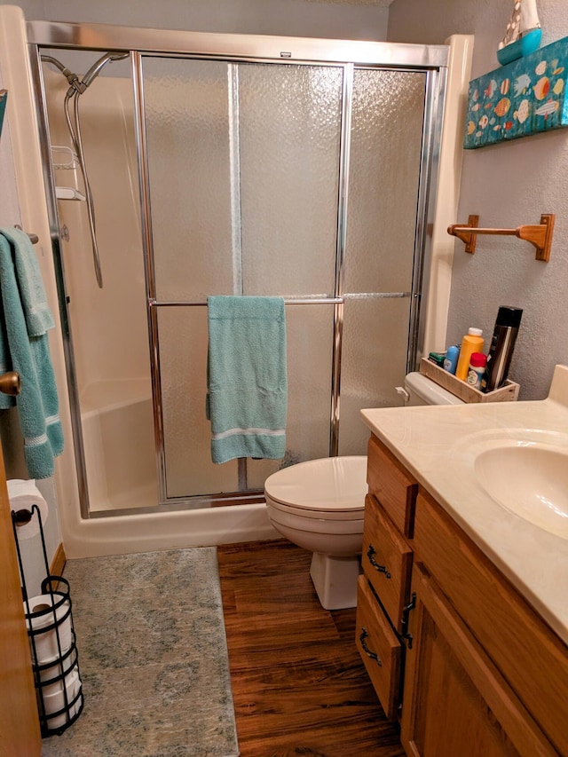 full bathroom with a shower stall, toilet, wood finished floors, a textured wall, and vanity