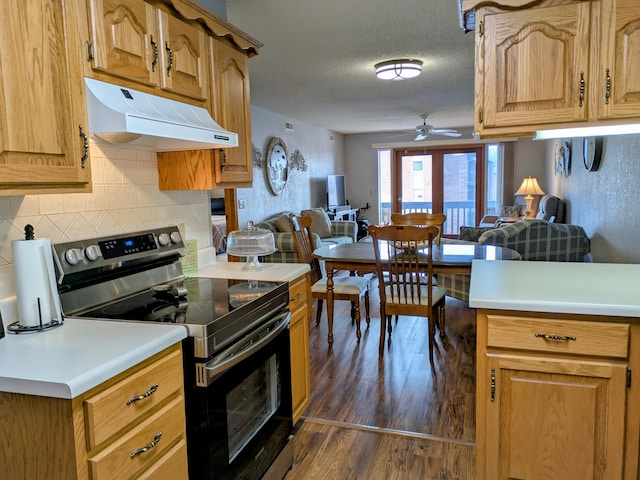 kitchen with dark wood-type flooring, stainless steel range with electric stovetop, under cabinet range hood, open floor plan, and light countertops