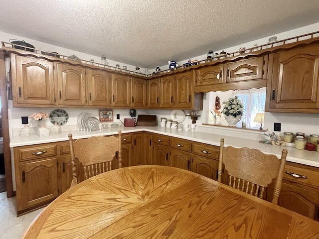 kitchen featuring a textured ceiling, brown cabinetry, and light countertops