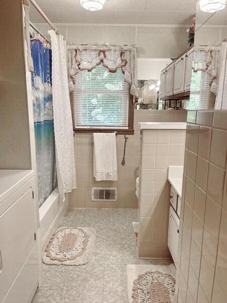 full bath with vanity, shower / bathtub combination with curtain, visible vents, washer / dryer, and tile walls