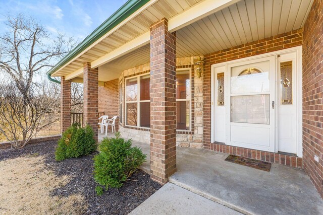 view of exterior entry featuring a porch and brick siding