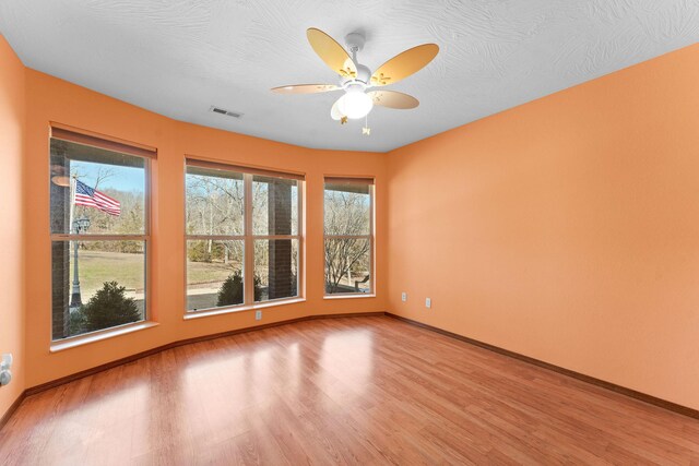 spare room featuring visible vents, ceiling fan, baseboards, wood finished floors, and a textured ceiling