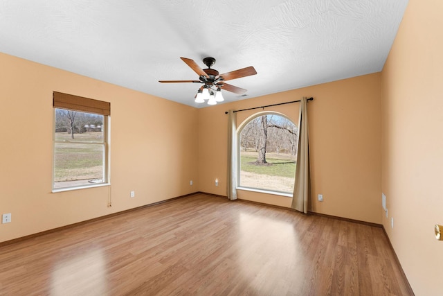 spare room featuring a ceiling fan, a healthy amount of sunlight, and light wood-type flooring