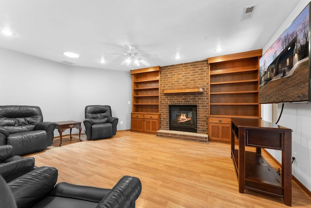 living room featuring visible vents, a ceiling fan, a fireplace, and light wood finished floors