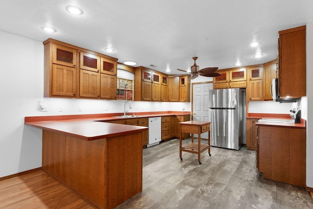 kitchen with a peninsula, a sink, stainless steel appliances, glass insert cabinets, and brown cabinets