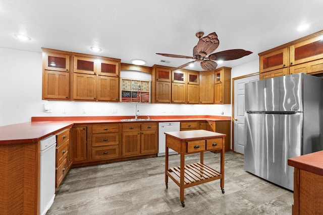 kitchen with brown cabinets, a peninsula, freestanding refrigerator, white dishwasher, and a sink