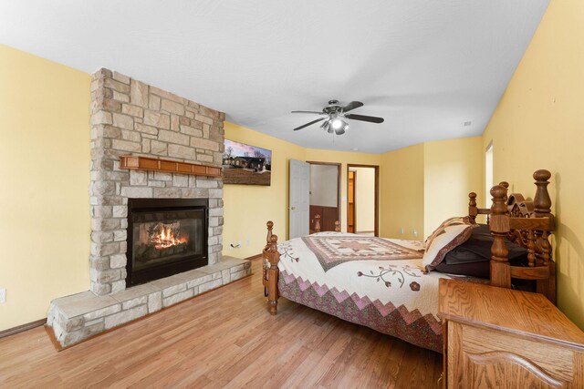 bedroom featuring a stone fireplace, ceiling fan, and wood finished floors