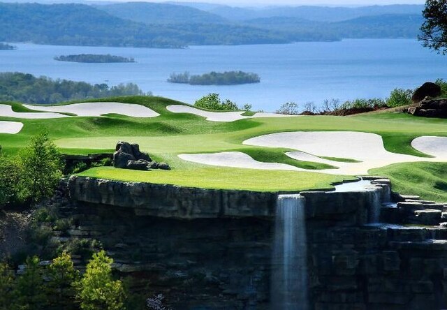 view of home's community with view of golf course, a lawn, and a water and mountain view