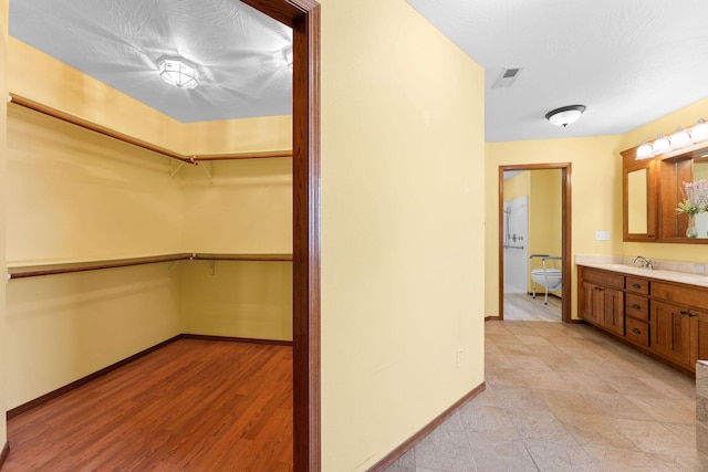 hall featuring light wood finished floors, visible vents, a textured ceiling, and baseboards