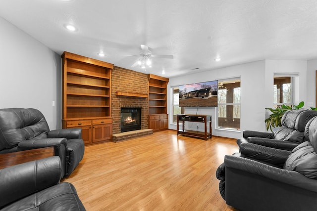 living area featuring built in shelves, light wood finished floors, recessed lighting, a textured ceiling, and a brick fireplace