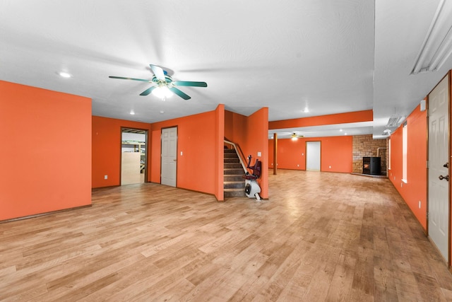 unfurnished living room featuring a brick fireplace, stairway, light wood-style floors, and ceiling fan