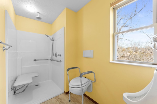 bathroom featuring wood finished floors, a shower, baseboards, and a healthy amount of sunlight