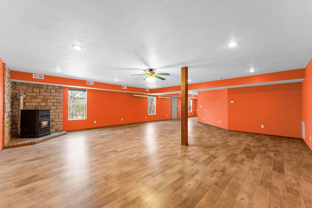 unfurnished living room with light wood finished floors, visible vents, a wood stove, a textured ceiling, and a ceiling fan