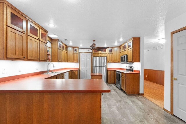 kitchen featuring appliances with stainless steel finishes, a peninsula, brown cabinetry, a ceiling fan, and a sink