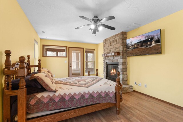 bedroom with a ceiling fan, wood finished floors, a fireplace, baseboards, and access to exterior