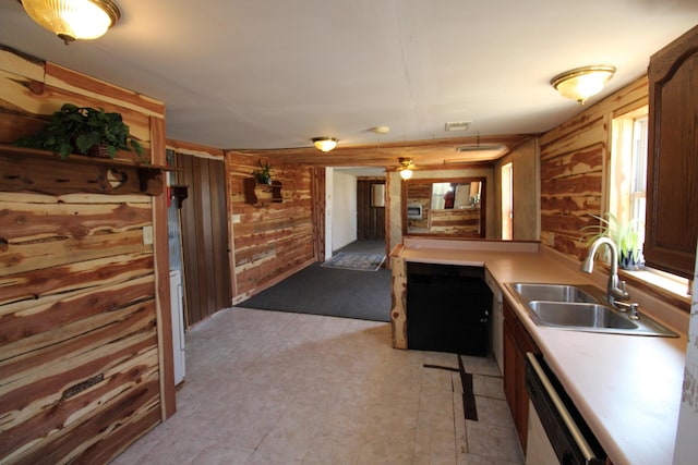 kitchen with a sink, wood walls, light countertops, and white dishwasher