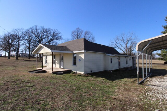 rear view of property featuring a detached carport, a lawn, and roof with shingles