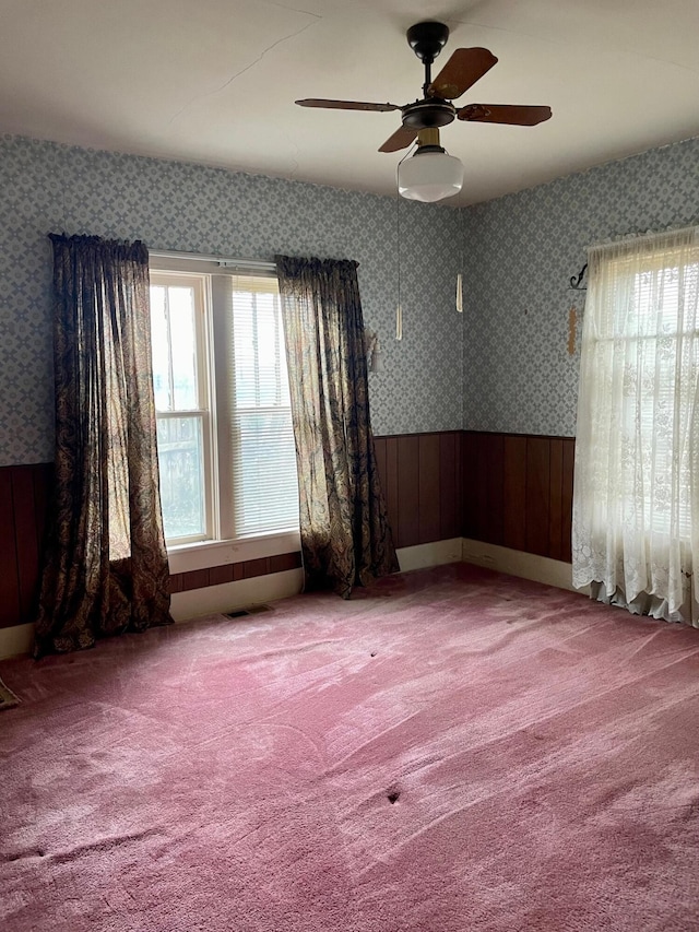 104 N High St, Neosho, MO 64850 - carpeted empty room with wallpapered walls, visible vents, a wainscoted wall, and ceiling fan