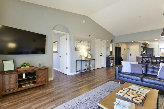 living area featuring arched walkways, wood finished floors, baseboards, and vaulted ceiling