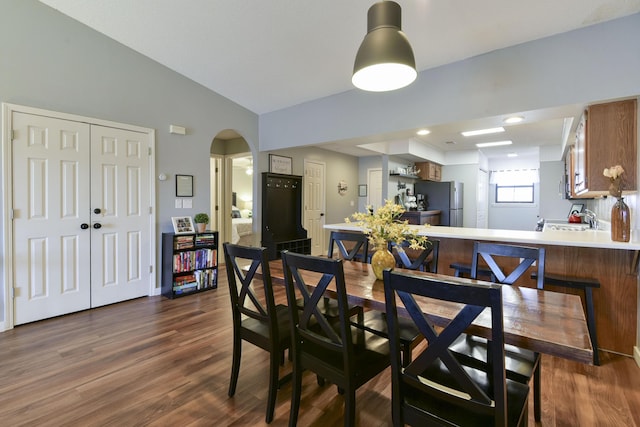 dining area with arched walkways, dark wood-type flooring, and lofted ceiling