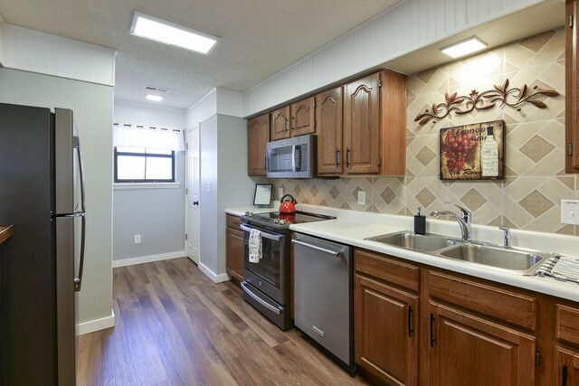 kitchen featuring dark wood-style floors, a sink, decorative backsplash, light countertops, and appliances with stainless steel finishes