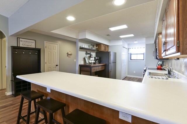 kitchen featuring a peninsula, dark wood-style flooring, freestanding refrigerator, and a sink