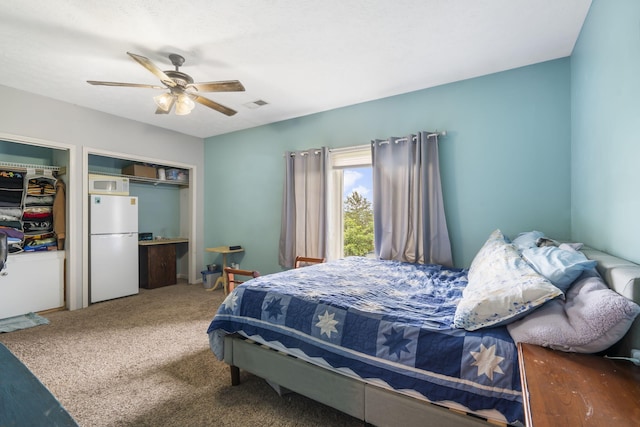 carpeted bedroom featuring a ceiling fan, visible vents, and freestanding refrigerator