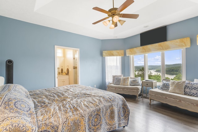 bedroom with a ceiling fan, a raised ceiling, wood finished floors, and ensuite bathroom