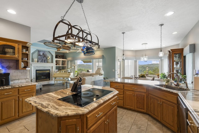 kitchen featuring dishwasher, brown cabinetry, a glass covered fireplace, black electric cooktop, and a sink