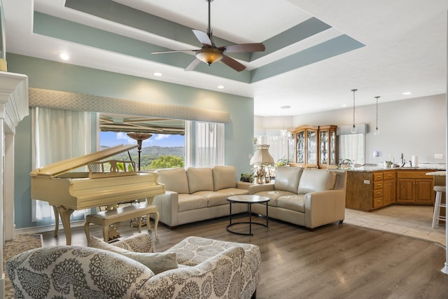 living room featuring a tray ceiling, light wood-style flooring, recessed lighting, and ceiling fan