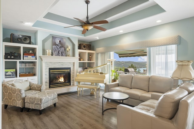 living room featuring a glass covered fireplace, a tray ceiling, wood finished floors, and ceiling fan