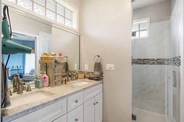 bathroom featuring a marble finish shower, backsplash, double vanity, and a sink