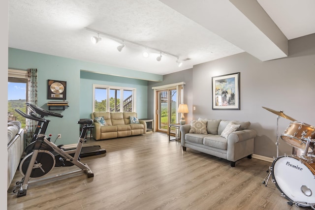 exercise area featuring track lighting, a textured ceiling, light wood-type flooring, and baseboards