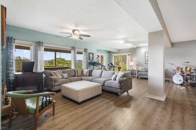 living area with ceiling fan, a textured ceiling, baseboards, and wood finished floors