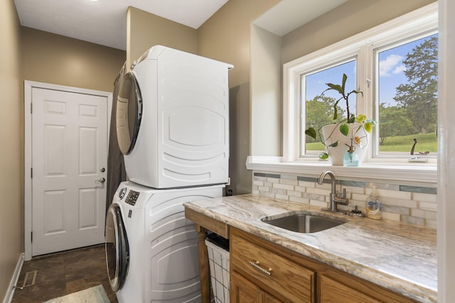 clothes washing area featuring cabinet space, stacked washing maching and dryer, baseboards, and a sink