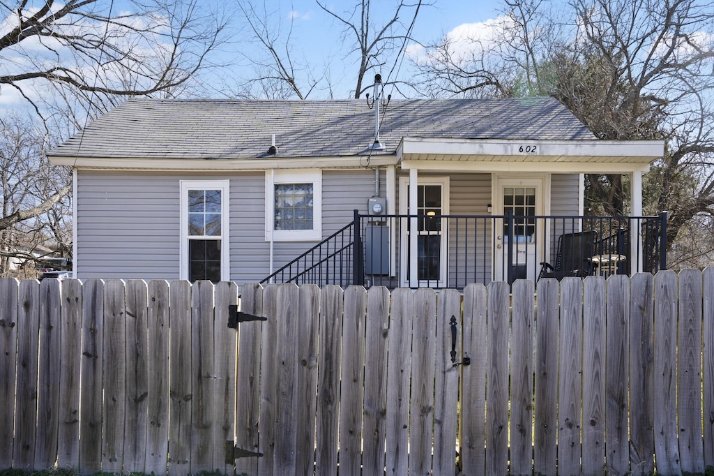 view of front of property featuring a fenced front yard, covered porch, a shingled roof, and a gate