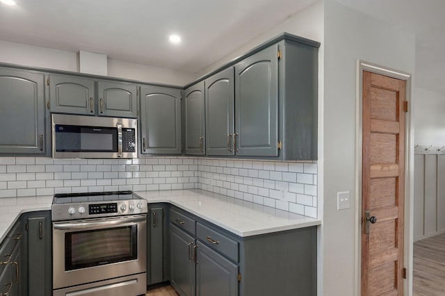 kitchen featuring gray cabinets, recessed lighting, appliances with stainless steel finishes, light wood finished floors, and decorative backsplash