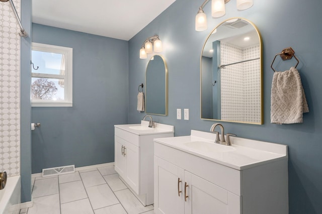 bathroom with visible vents, two vanities, walk in shower, and a sink