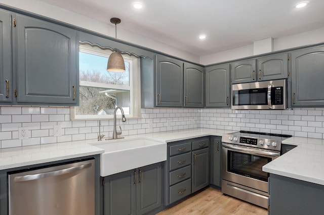 kitchen with light wood-type flooring, gray cabinets, a sink, tasteful backsplash, and stainless steel appliances