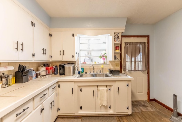 kitchen featuring backsplash, baseboards, tile counters, light wood-style floors, and a sink