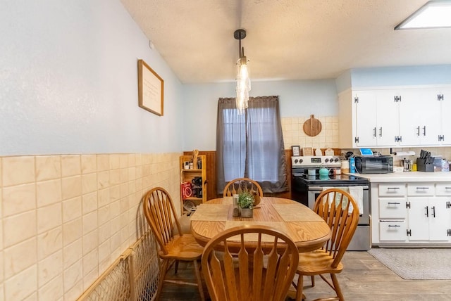 dining room with tile walls, a toaster, light wood finished floors, and a textured ceiling