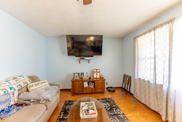 living room featuring visible vents, light wood-style flooring, a textured ceiling, and baseboards