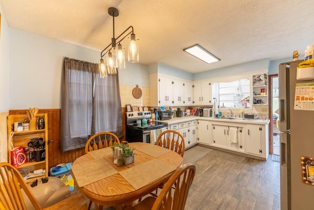 dining area featuring light wood-type flooring, a textured ceiling, and a wainscoted wall