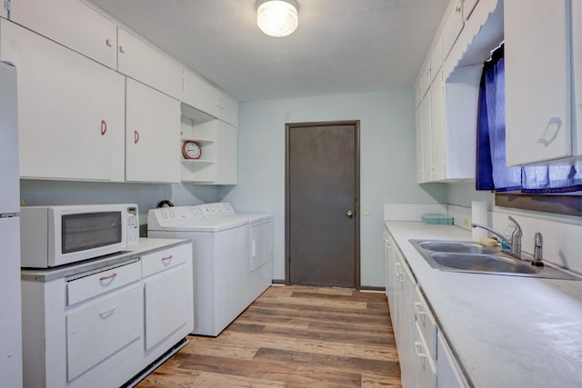 kitchen with washer and dryer, white microwave, white cabinetry, and a sink